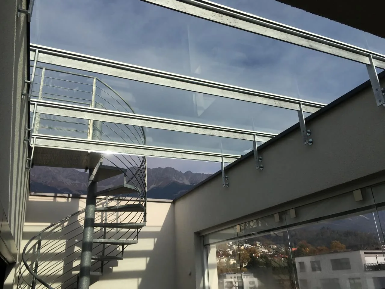 Glasdach über einer Dachterrasse, dahinter eine Wendeltreppe und das Bergpanorama