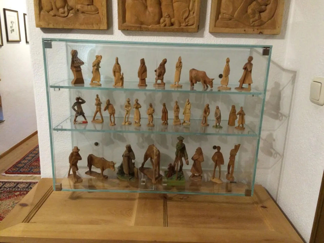 Wandvitrine aus Glas mit geschnitzten Holzfiguren