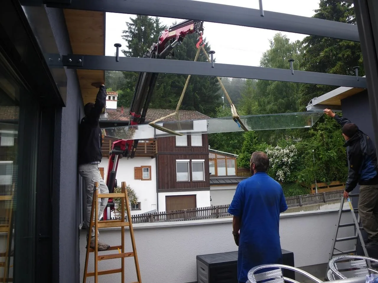 Drei Monteure setzen mit einem Kran eine Glasscheibe in ein Dachtragwerk
