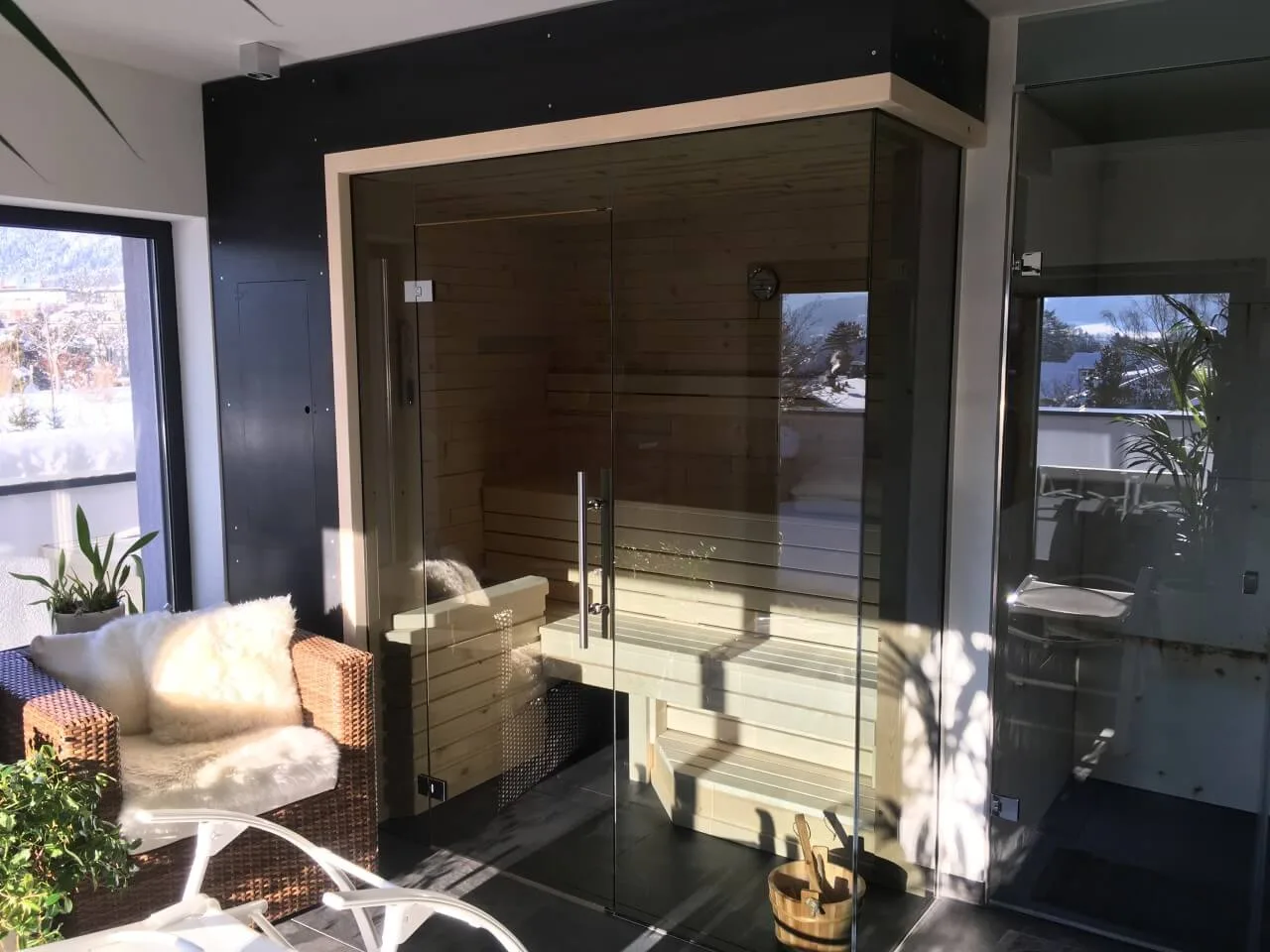 Sauna mit Ganzglasfront, daneben eine Glasdusche, im Fenster Schnee und Berge